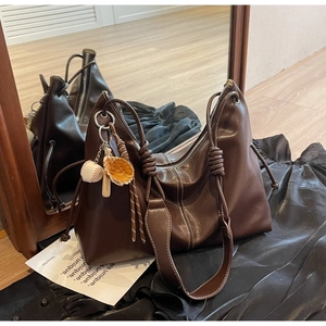 Detail of dark brown leather tote bag with braided handles and baseball glove charm