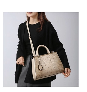 Detail of beige crocodile pattern handbag featuring a top handle and adjustable shoulder strap