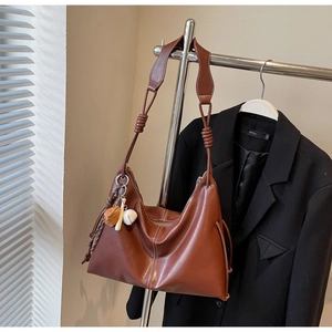 Brown leather tote bag with wide knotted strap and sports charm on a hanging display