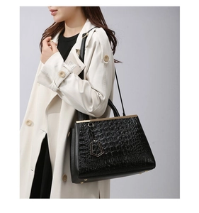 Detail of black crocodile texture bag with gold hardware worn on white coat