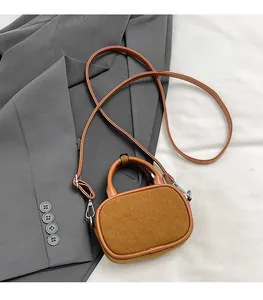 Detail view of brown suede mini crossbody bag with leather handle on grey blazer