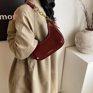 Détail du sac croissant bordeaux avec bandoulière chaîne et trench-coat beige