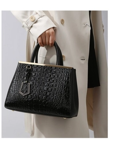 Close-up of black crocodile pattern leather handbag with gold metal charms on model