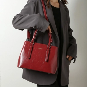Deep red patent leather tote bag with gold lettering shown by a model in a grey suit