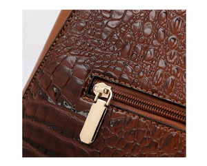 Close-up of golden zipper and dark brown crocodile embossed leather on handbag