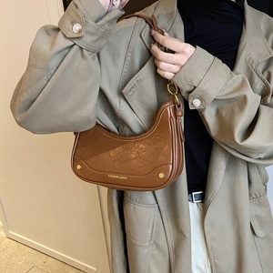 Sac hobo marron en simili cuir ciré vintage avec rivets porté par un mannequin en extérieur