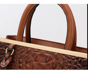 Detail of brown crocodile embossed leather handbag with golden metal hardware accents