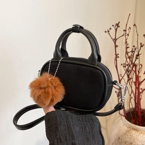 Detail of black oval handbag with matte suede texture and plush brown pompom charm
