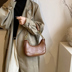Sac demi-lune marron en similicuir avec chaîne dorée porté par un mannequin