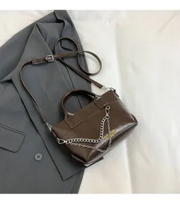Détail d'un sac bandoulière marron avec chaîne argentée et poignée supérieure élégante
