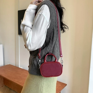 Detail of burgundy stitching on a small faux suede crossbody bag with silver hardware