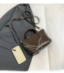 Détail du sac à bandoulière marron foncé avec chaîne argentée et sangle sur une veste grise