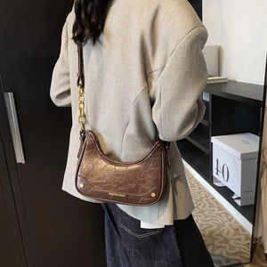 Détail d'un sac demi-lune marron foncé avec texture vintage et chaîne dorée