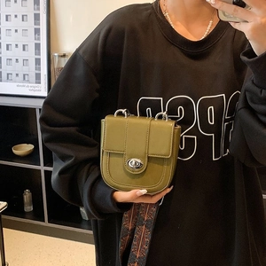 Detail of dark green saddle bag with silver oval twist lock and patterned wide strap