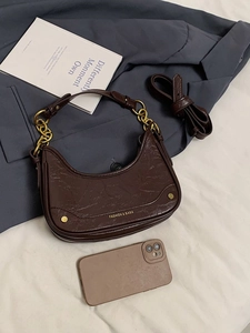 Détail d'un sac demi-lune marron foncé avec chaîne dorée et finition en cuir texturé