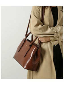 Detail of a brown glossy leather tote bag with dual handles and adjustable shoulder strap