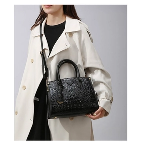 Detail of black crocodile texture handbag with triangle metal logo and golden hardware