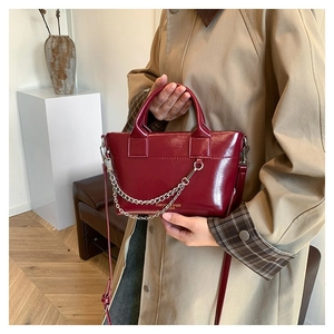 Détail du sac à main bordeaux en cuir brillant avec chaîne dorée et bandoulière amovible