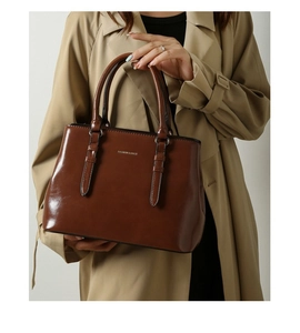 Close-up of dark brown glossy leather tote bag with buckle details and silver logo