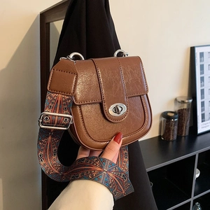 Close-up of brown vintage saddle bag featuring a silver twist lock and ethnic woven strap
