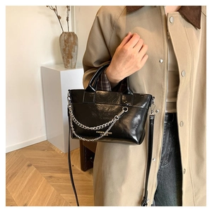 Détail du sac en cuir verni noir avec chaîne argentée et logo de mode imprimé