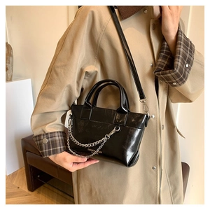 Détail du sac à main noir brillant avec chaînes argentées et logo de mode doré