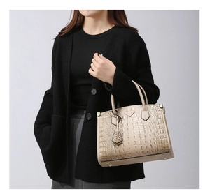 Detail of beige crocodile pattern handbag with triangular logo and leather charm