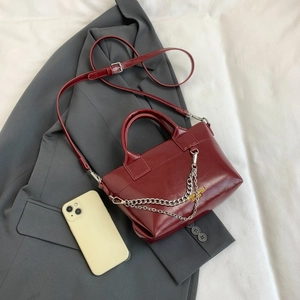 Détail d'un sac à main bordeaux brillant avec chaîne argentée sur blazer gris