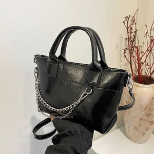 Détail d'un sac cabas en cuir noir brillant avec chaîne argentée et logo mode