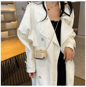 Detail of a gold metallic crossbody bag with vertical ribs on a white trench coat