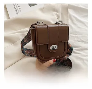 Detail of retro brown leather bag featuring a gold metal lock and colorful wide woven strap