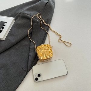 Detail of a mini gold textured metal crossbody bag shown with a smartphone for scale