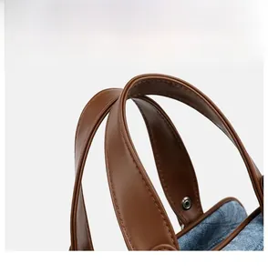 Close-up of brown leather handle on blue denim handbag with reinforced stitching