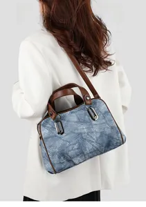 Denim blue crossbody bag with brown leather strap worn over a white blazer
