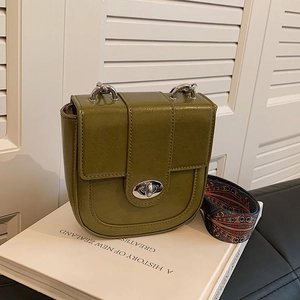 Retro grass green saddle bag with woven wide strap on a white book and shutter background