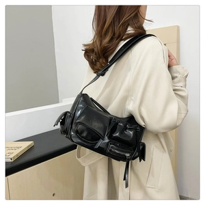 Détail d'un sac à bandoulière brillant noir avec plusieurs poches sur un manteau beige