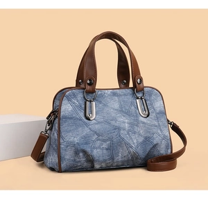Detail of vintage denim crossbody bag featuring brown leather trim and metal U-shaped buckle