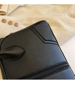 Close-up of black litchi grain leather texture and handle stitching on a shoulder bag