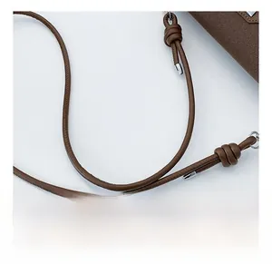 Detailed view of the brown knotted faux leather strap with silver hardware on a crossbody bag