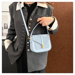 Detail of light blue shoulder bag with woven flap and gold buckle on a model