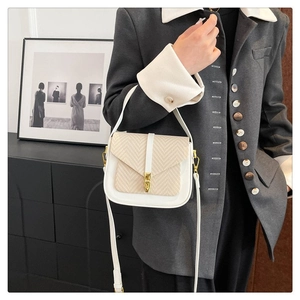 Model wearing beige woven crossbody bag with gold buckle over a grey blazer