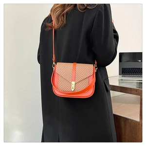 Detail of orange leather and woven fabric shoulder bag with golden clasp worn by model