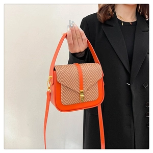 Detail view of orange leather crossbody bag with herringbone pattern and gold metal lock