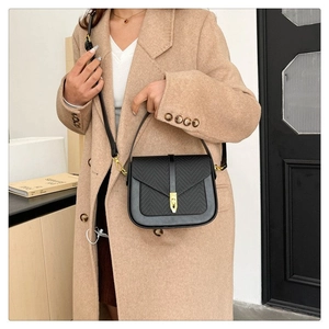 Detailed view of black woven shoulder bag with gold clasp shown on model shoulder