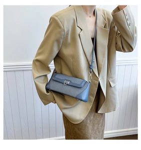 Detail of blue textured crossbody bag with silver twist lock on model in khaki blazer