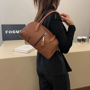 Detail of brown pebbled leather texture and silver zipper on a minimalist Boston handbag