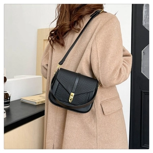 Crossbody black bag with woven flap detail and golden metal clasp on a female model