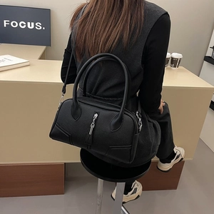 Detail view of black pebble leather handbag featuring silver hardware and top handles
