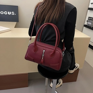 Detail of burgundy lychee grain leather boston bag worn by a model in a minimal setting