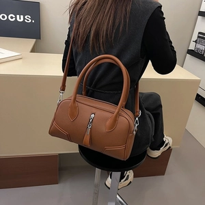 Close-up of brown pebbled leather bag with silver zipper and metal pendant detail